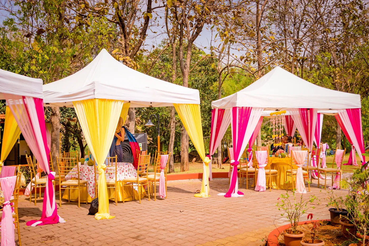 White tents with pink and yellow drapes shade seating on a brick paved courtyard