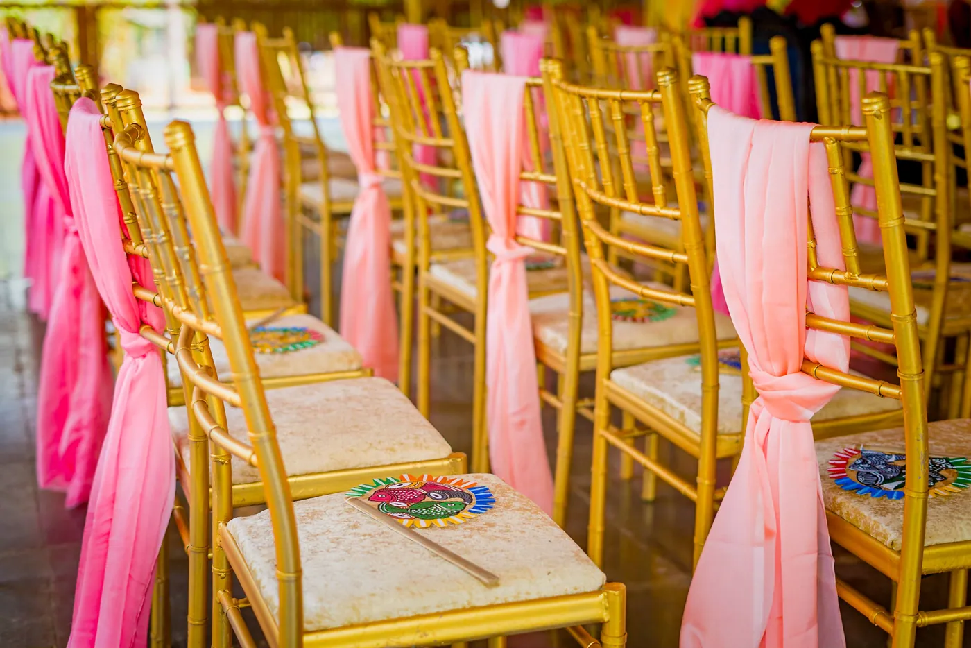 Gold chairs with pink fabric bows stand in rows at the ceremony hall