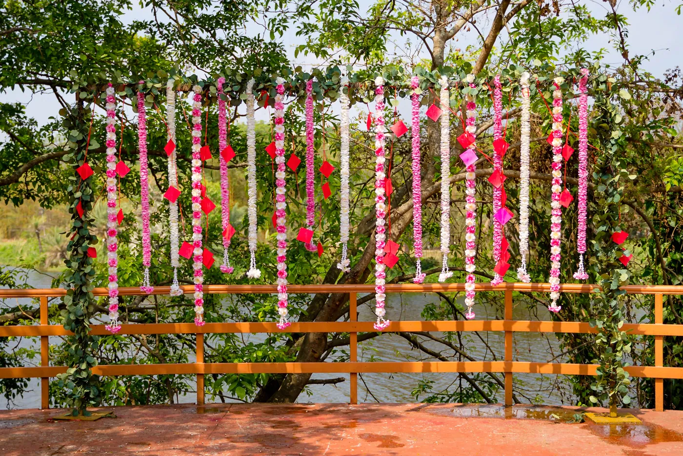 A backdrop of hanging pink and white flower strings stands above a wooden railing by a lake