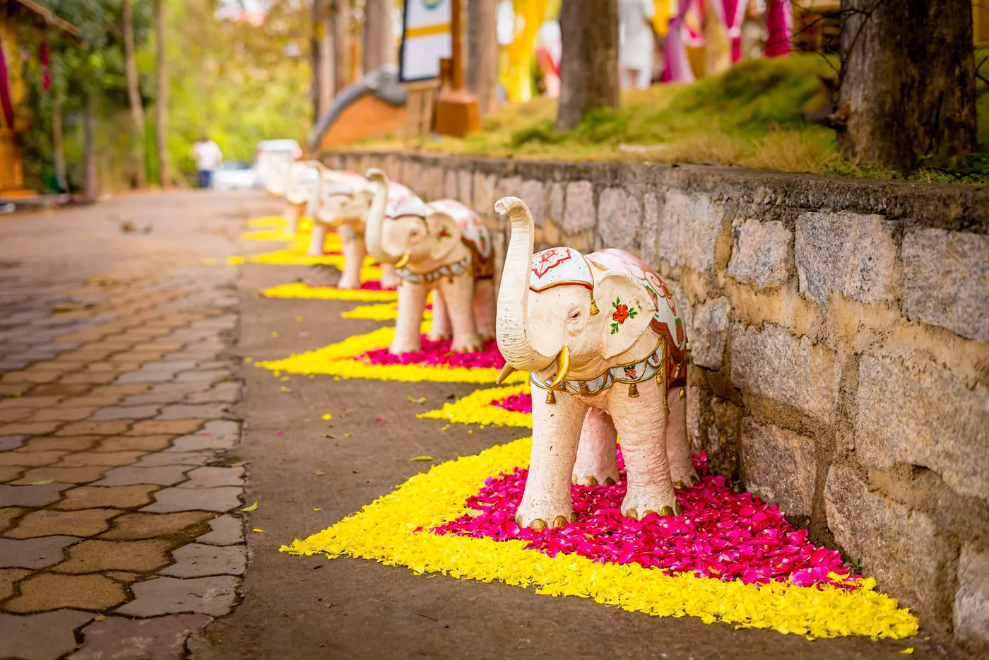 A stone elephant stands on a path lined with yellow and pink flower petals