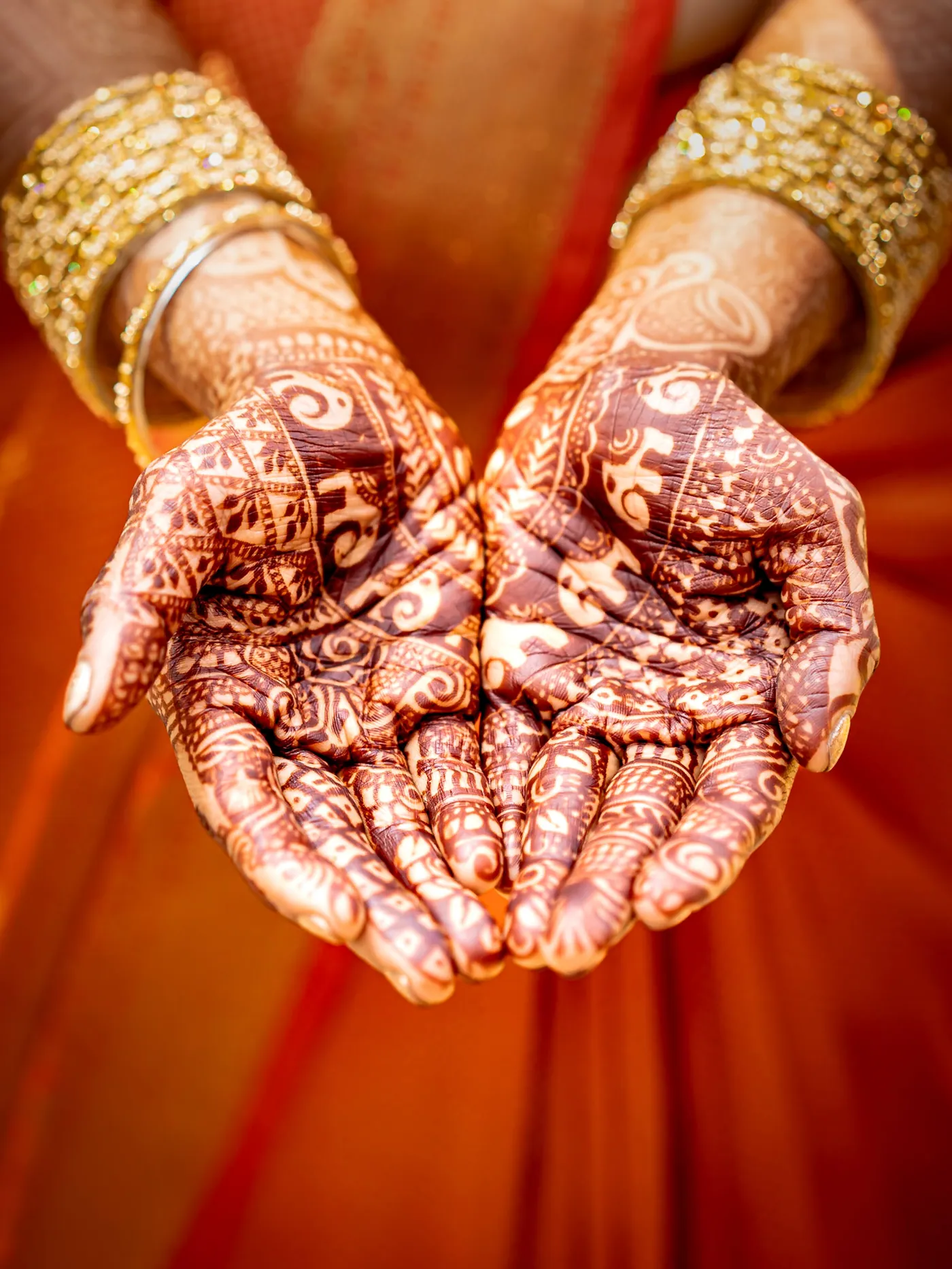 Close view of two cupped hands with intricate henna against an orange sari