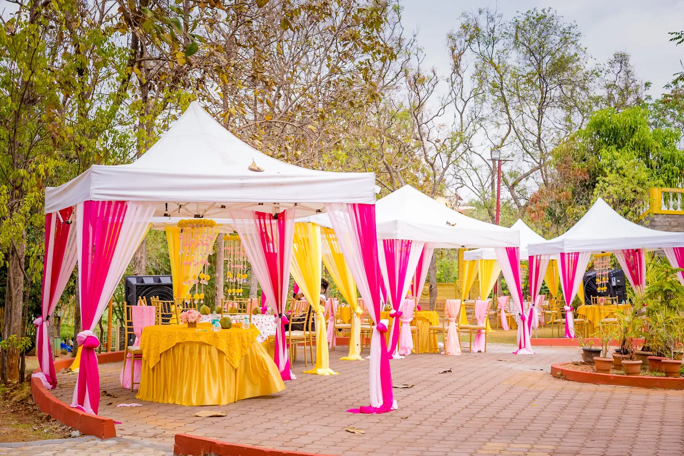 A white tent with pink and yellow drapes stands on a paved yard
