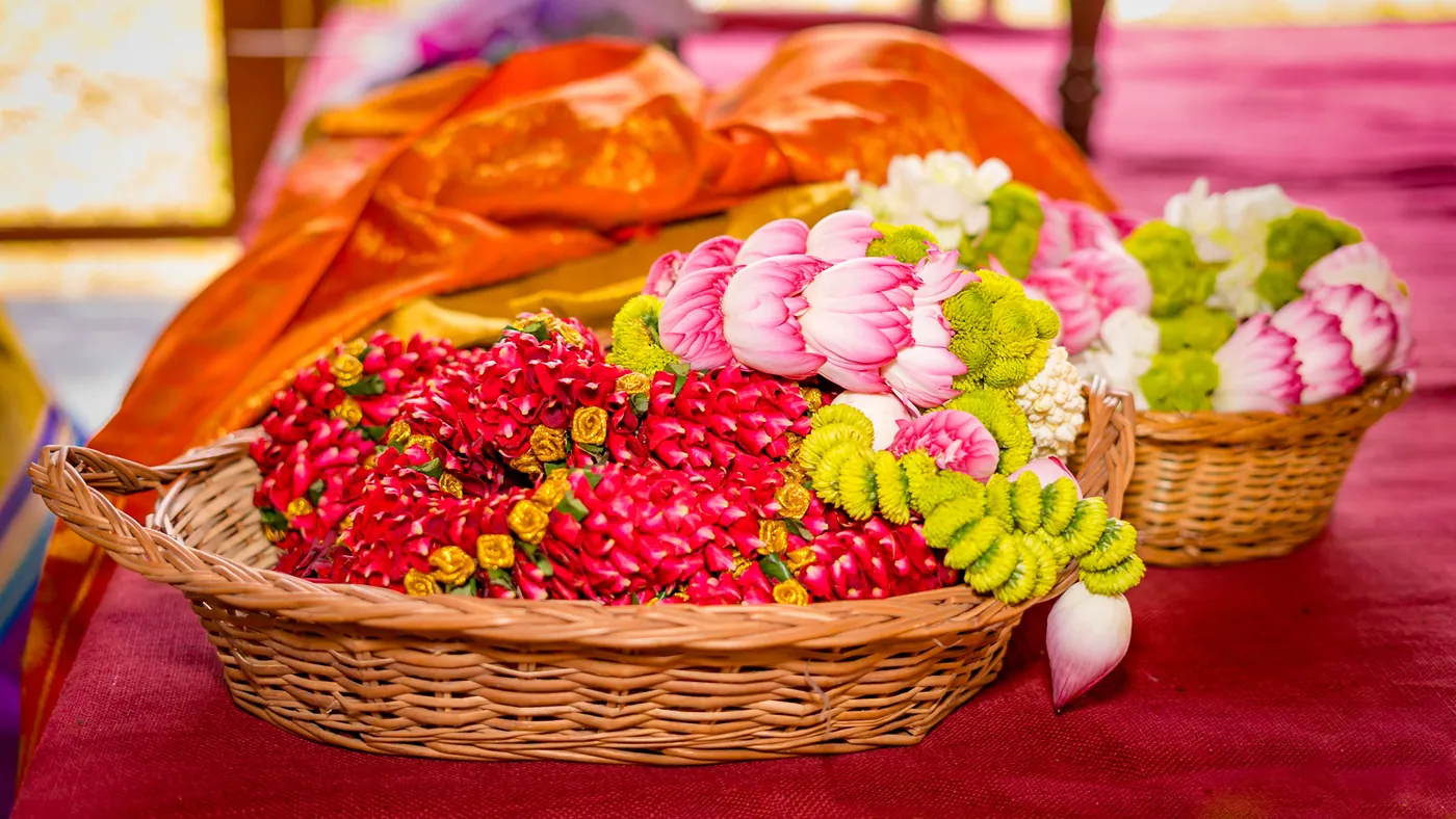 A basket of red and pink flowers and garlands sits on a red cloth