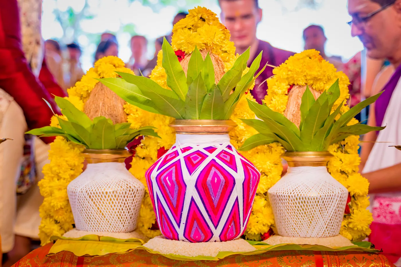 A pink and white decorated pot between two white pots, framed by yellow flowers