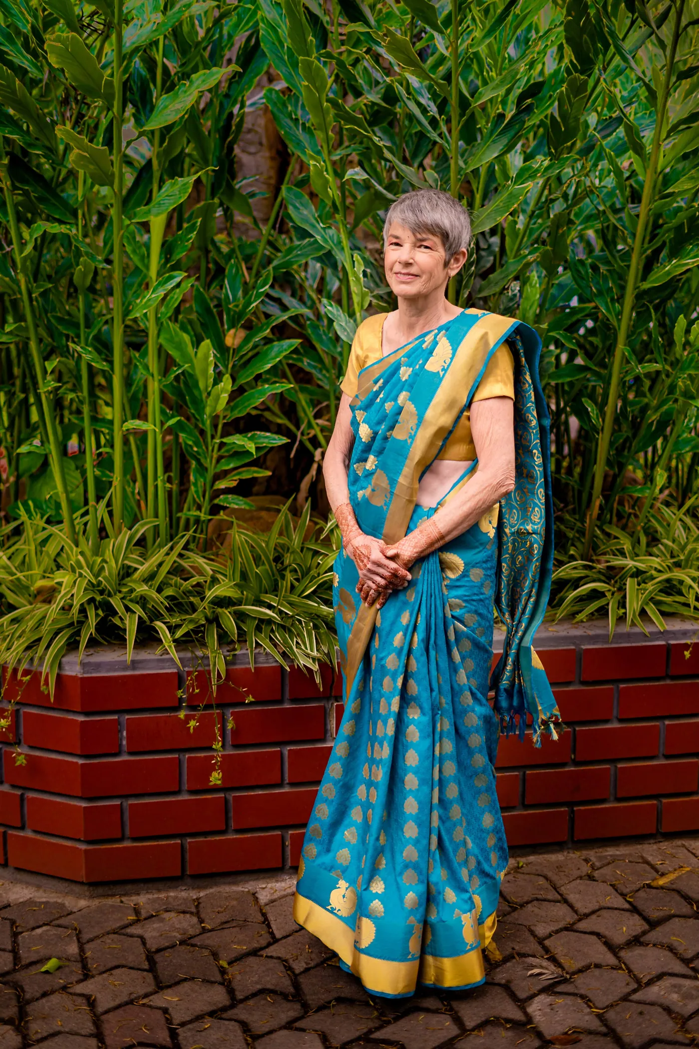 Stefan's mother in a teal and gold sari in front of green leaves