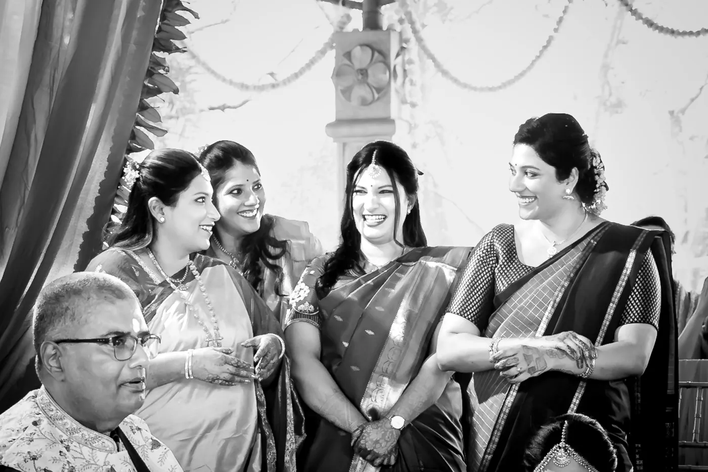 Black and white of smiling guests, one man in glasses sitting among laughing women