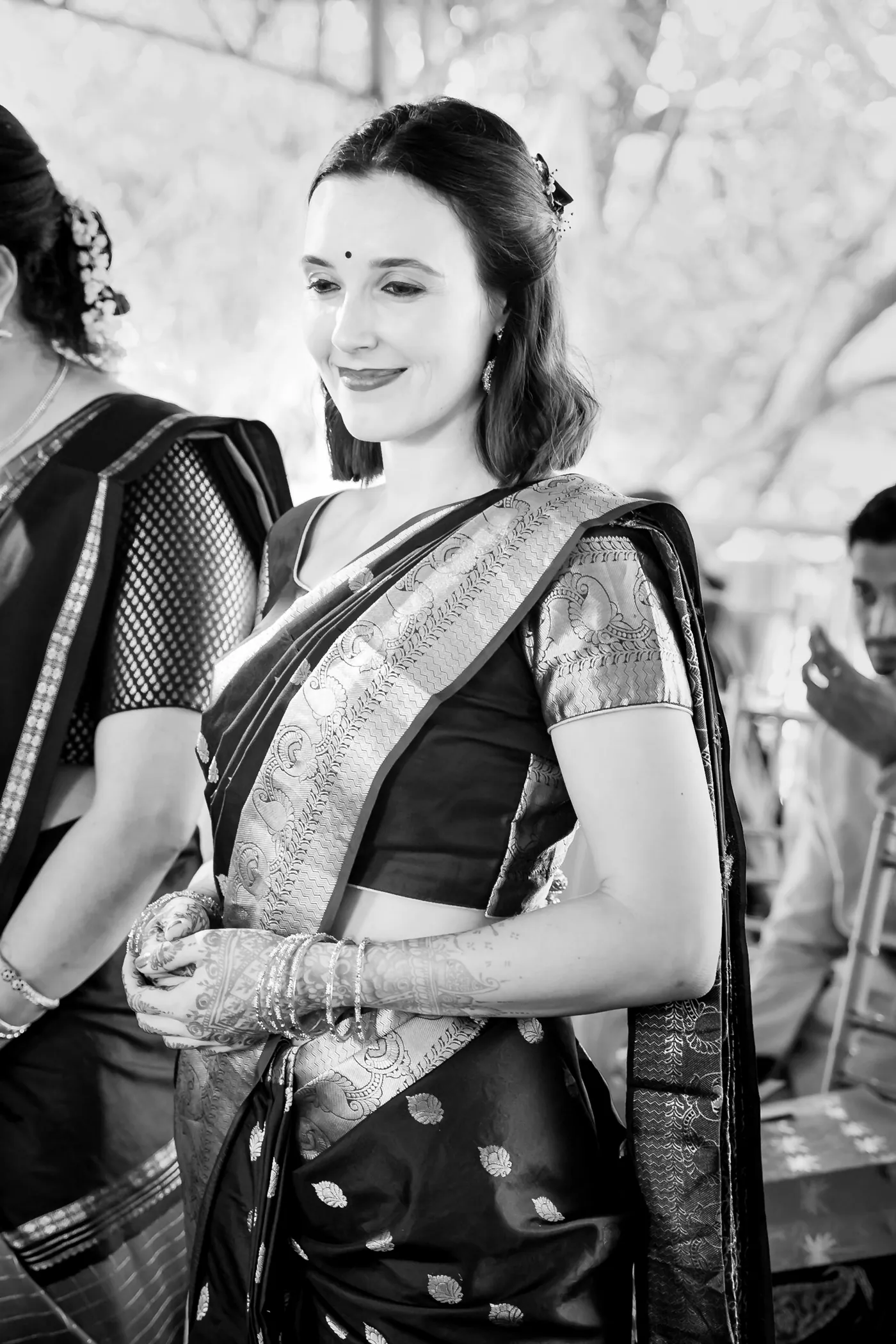 Black and white of a woman in a sari smiling softly as guests stand behind her