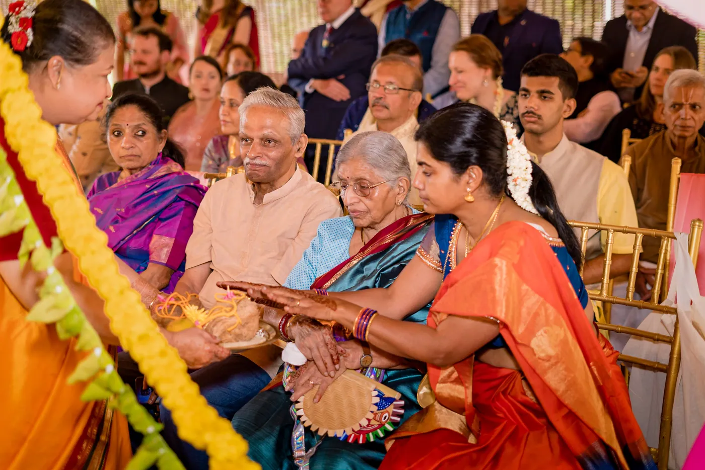 Family and elders sit close together, one older woman looking on with a quiet smile