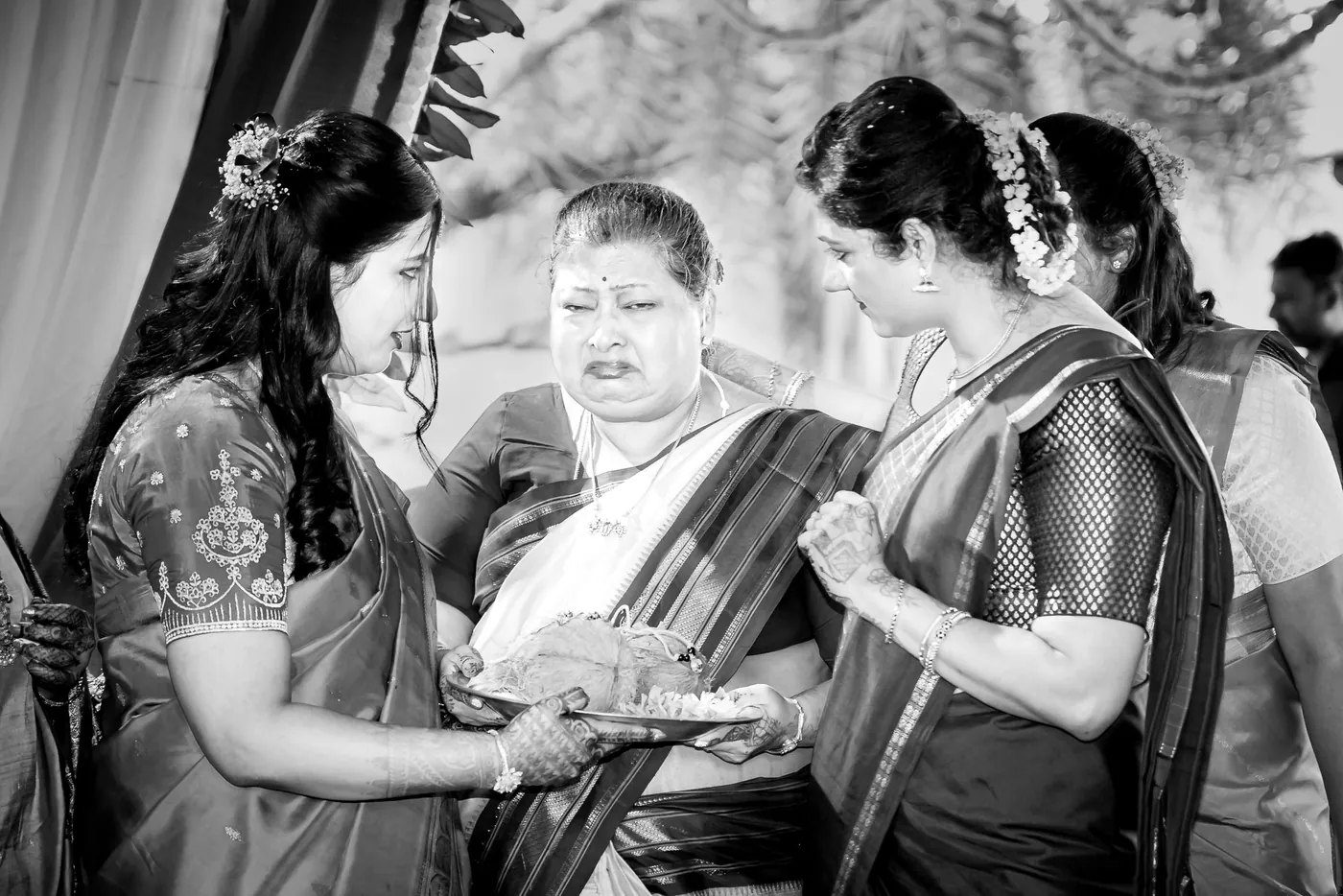 Black and white of a woman covering her face with her hand, moved between two women