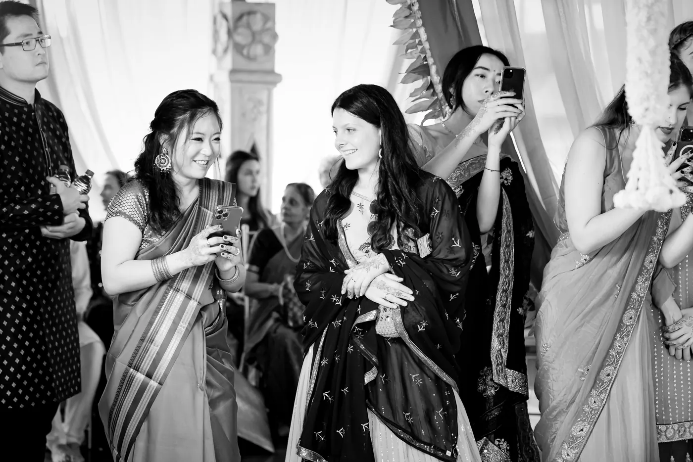 Black and white of guests holding phones and smiling as they watch the ceremony