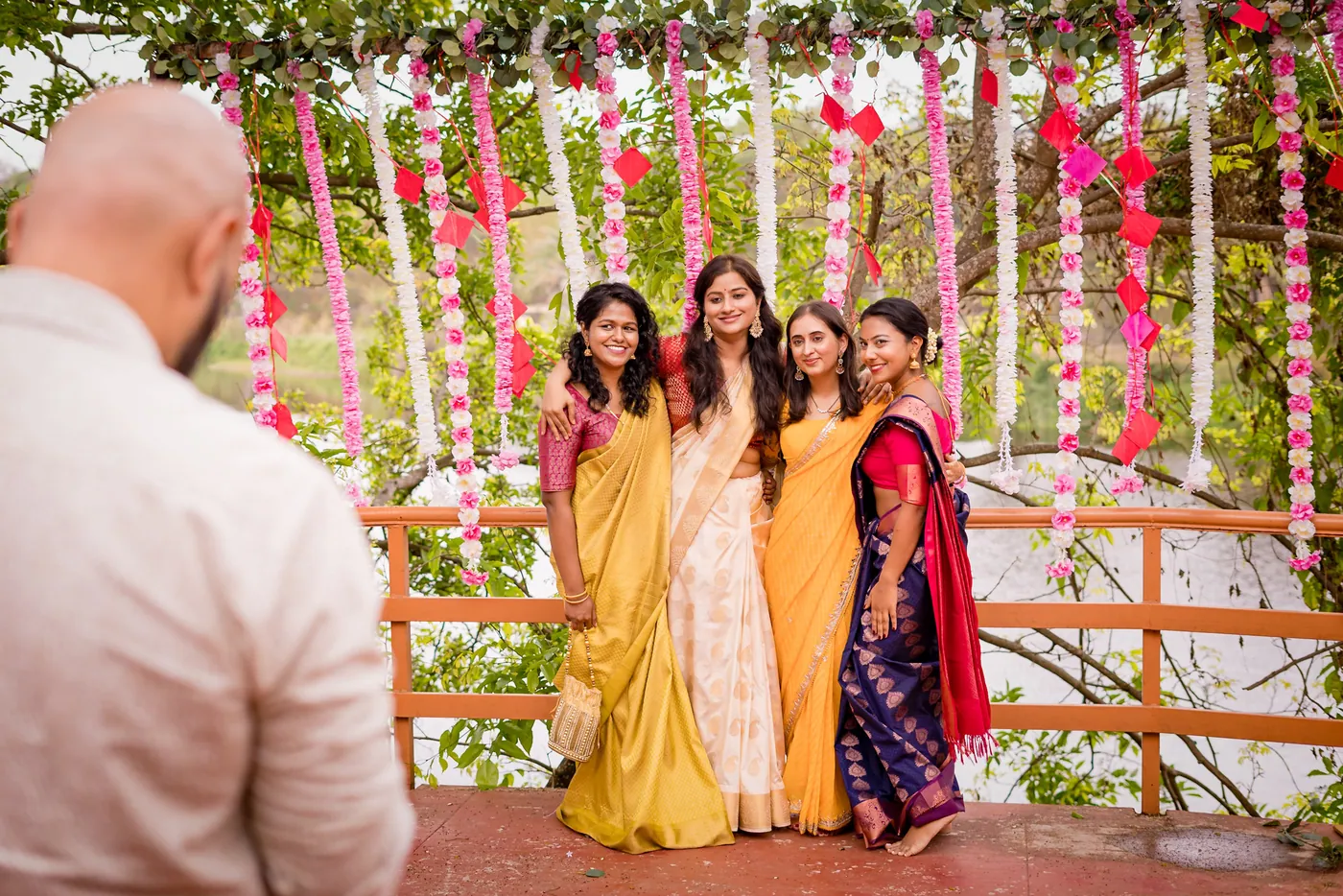 Four women in yellow and cream traditional clothes pose in front of flower strings