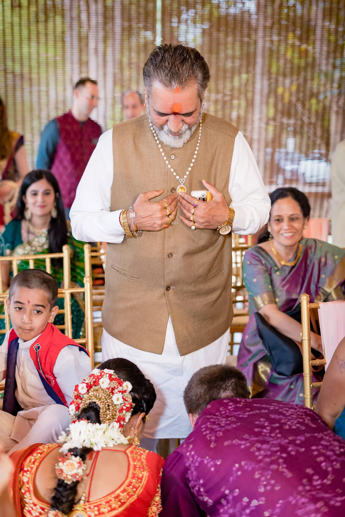 A man in a brown vest holds a necklace while family and children sit around him