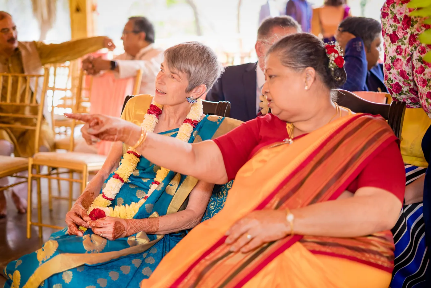 An older woman in teal and a woman in orange laugh as one points in conversation