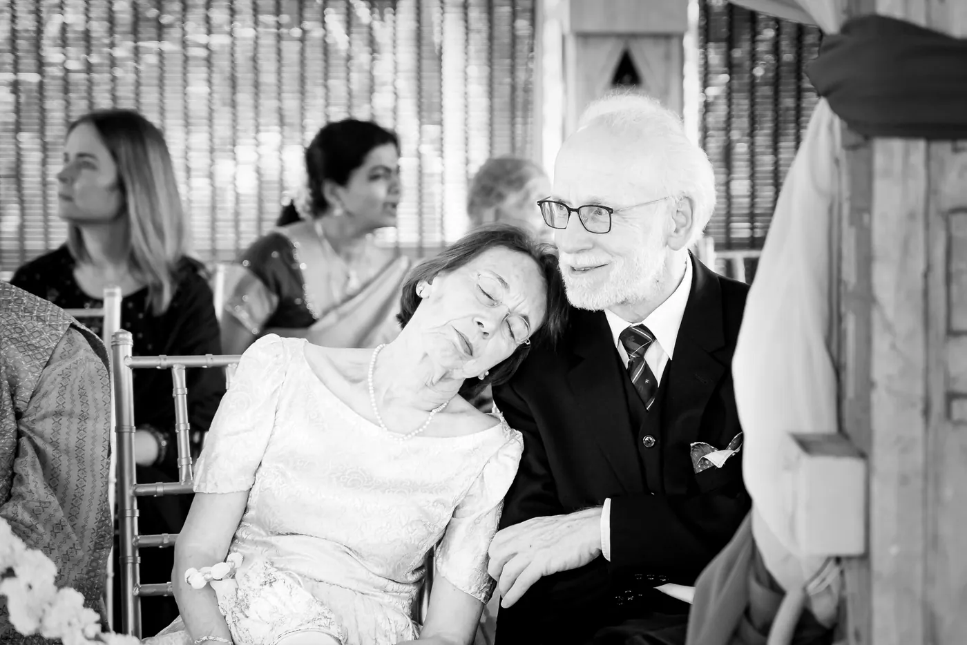 Black and white of an older woman resting her head on a man in a suit