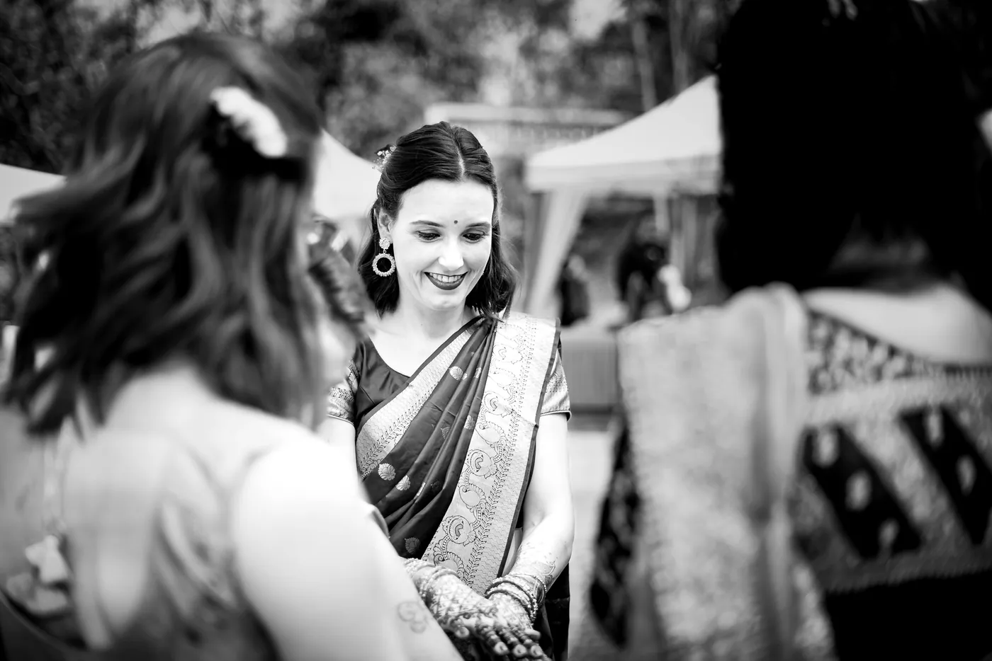 Black and white of Stefan's sister in a sari smiling at her henna decorated hand as guests pass in front