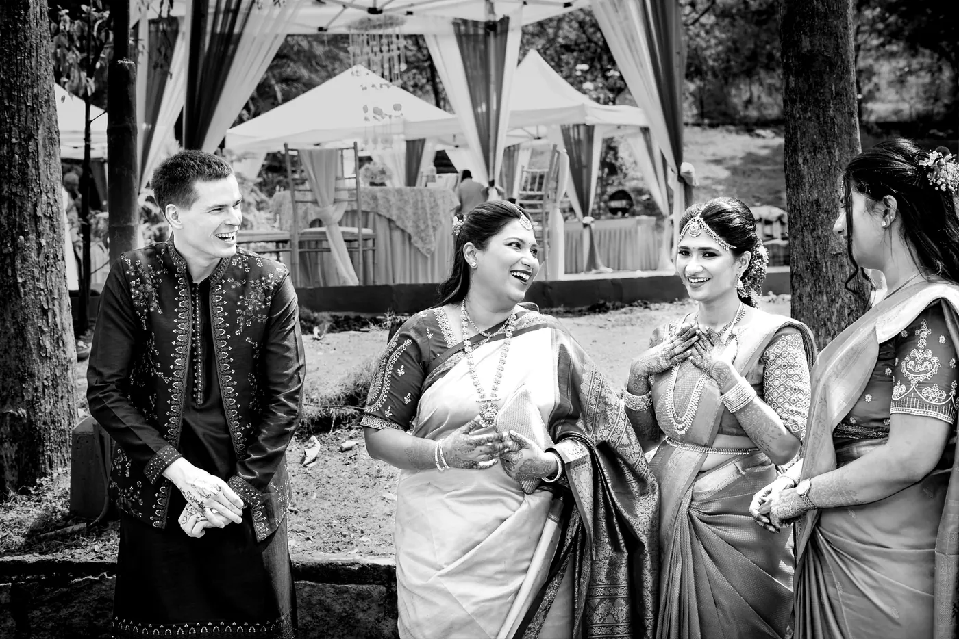 Stefan laughs beside Medha and two women in saris who chat and giggle in front of white tents