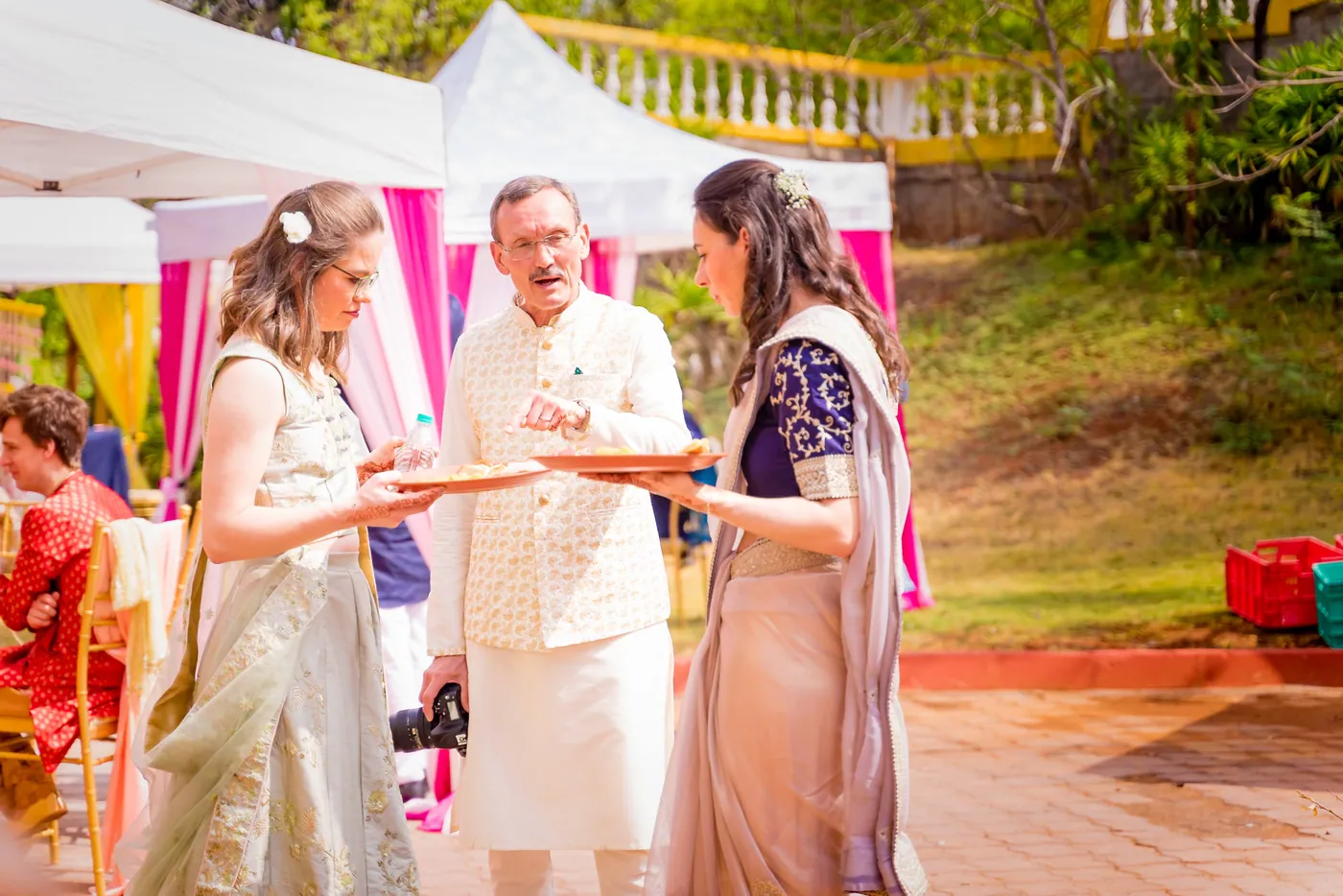 A guest and a man in a cream waistcoat with a camera stand under tents at the venue
