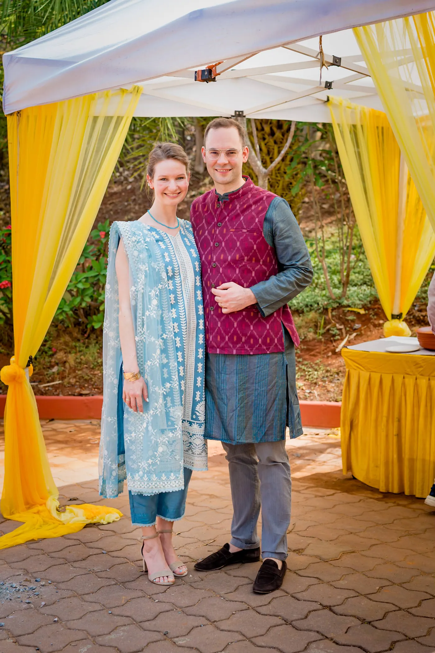 A woman and a man in a magenta waistcoat stand together beneath yellow and white drapes
