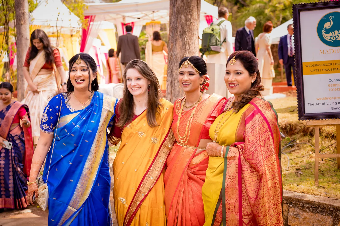 Four women in bright silk saris smile in a group at the entrance of the venue