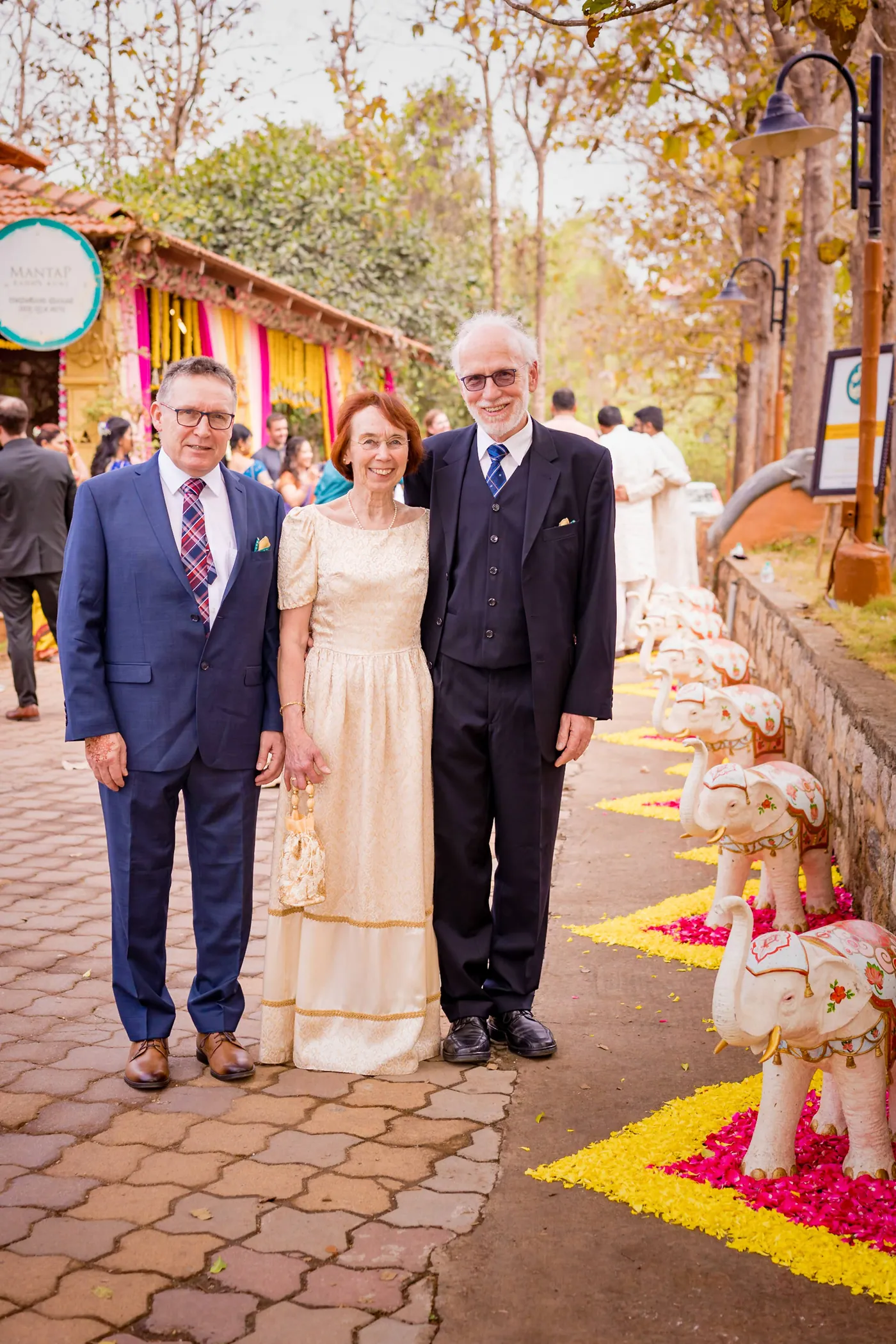 Three guests in formal and traditional clothes stand along a flower-petal path