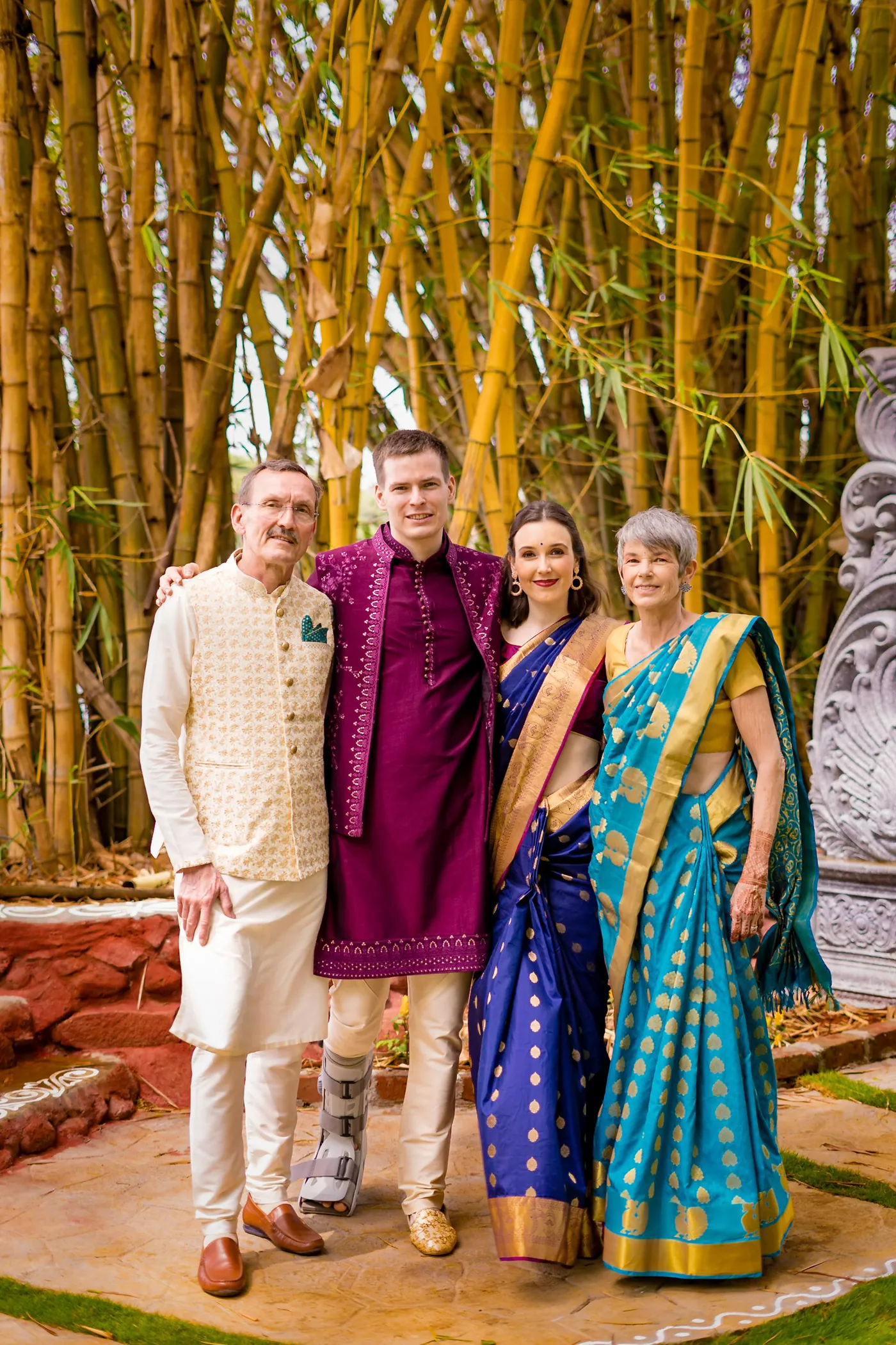 Four guests pose among bamboo, one man in a cream kurta and one in magenta