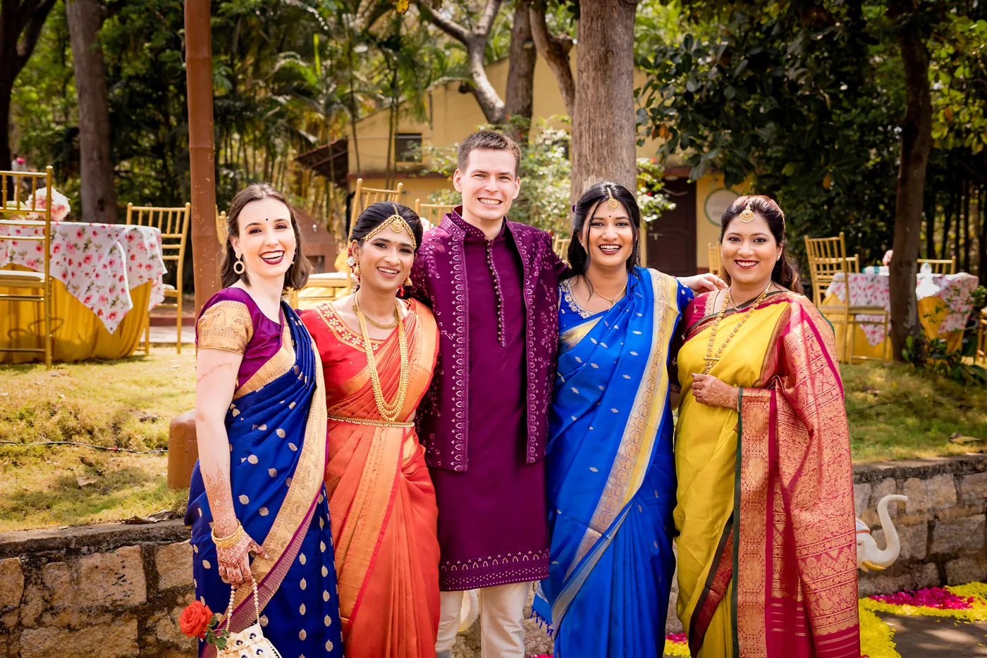 Stefan in a magenta jacket stands with four women in bright silk saris