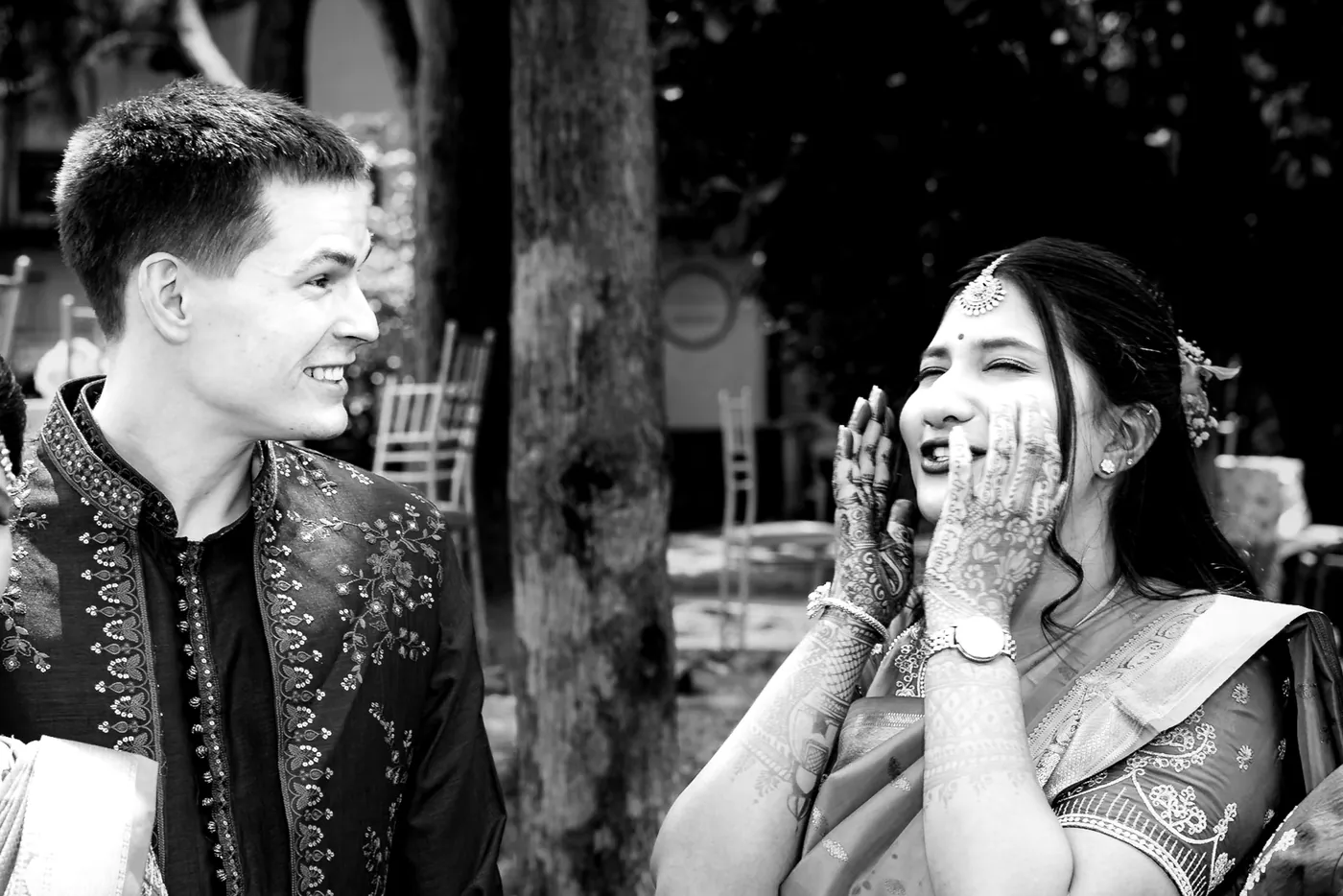 Black and white of Stefan smiling sideways while a woman laughs with her hands on her face