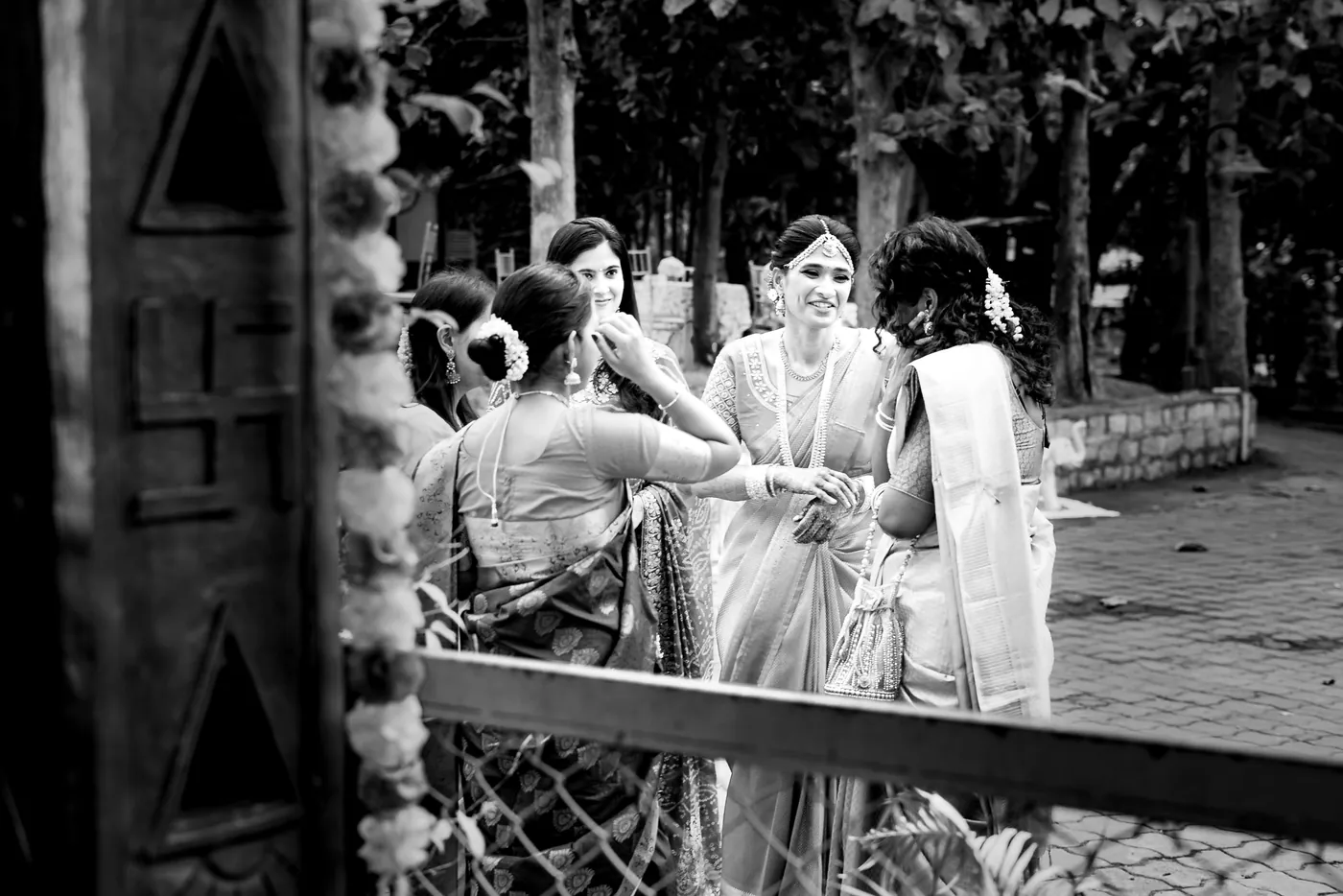 Black and white of women in saris chatting by a carved wooden door and railing