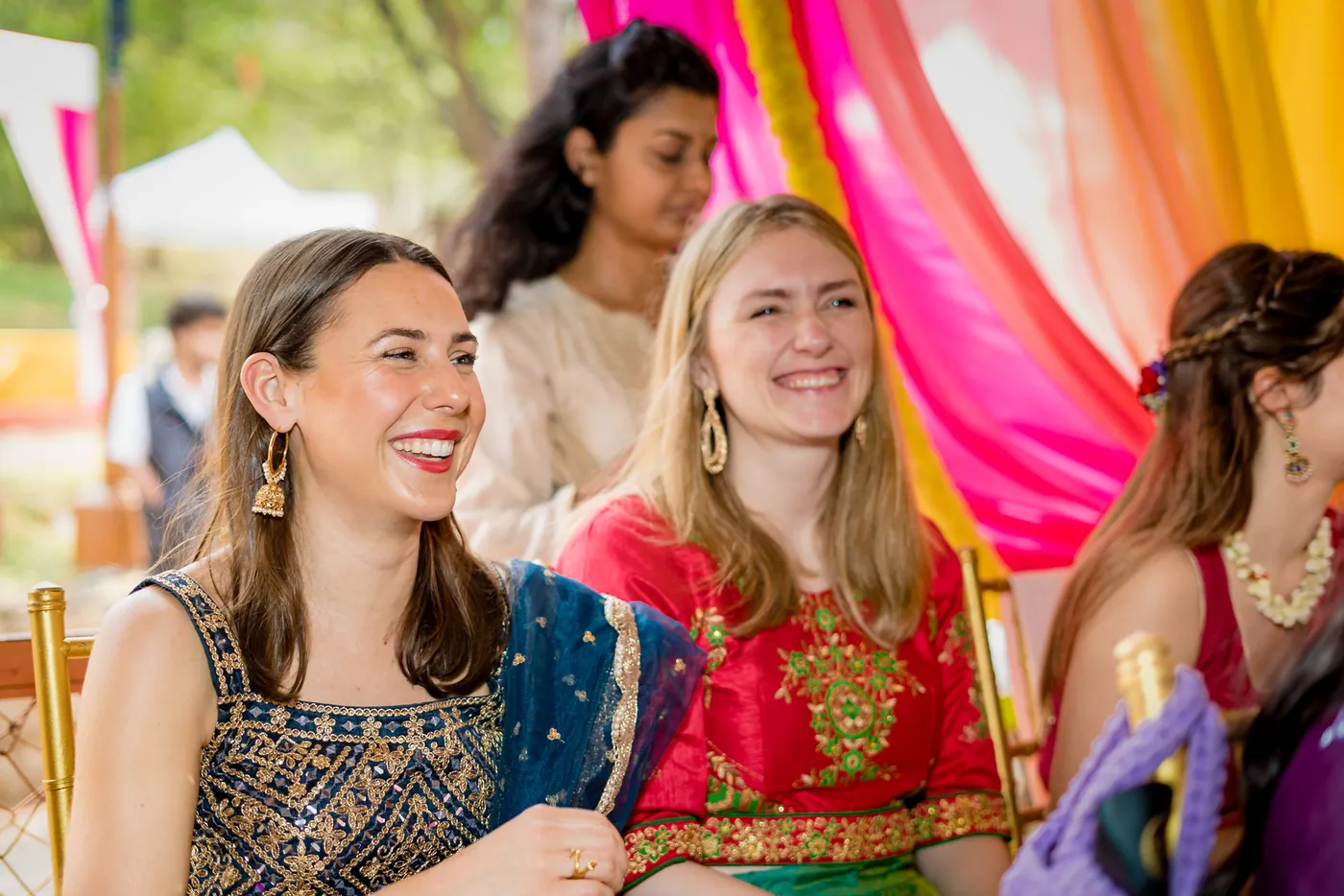Three young women smile and laugh together in front of pink and yellow drapes