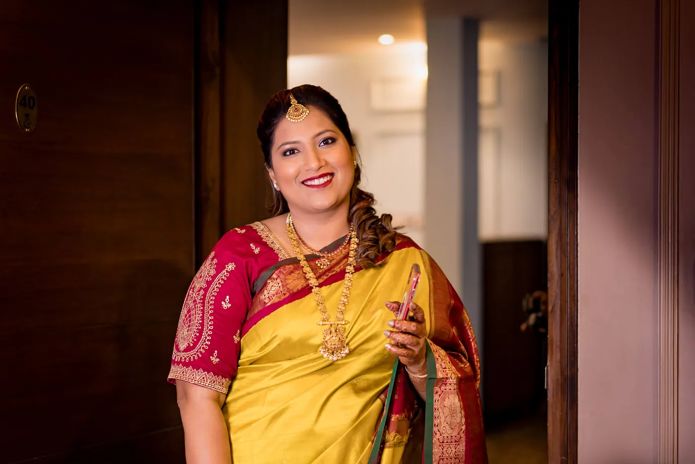 Medha's sister in a yellow sari smiles in a doorway of a wooden room