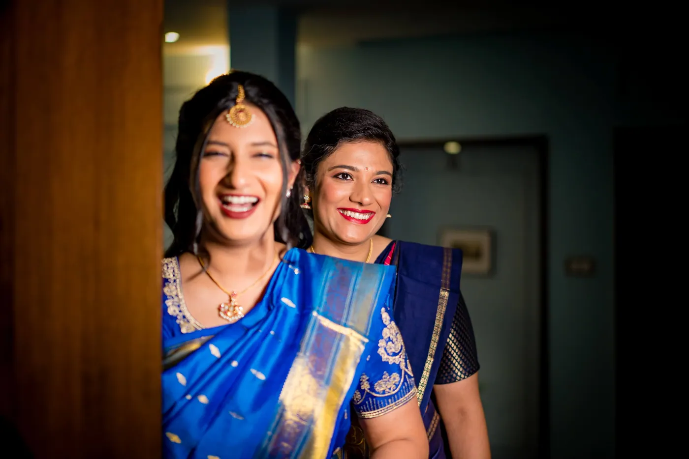 Medha's two sisters laugh together in a dim doorway