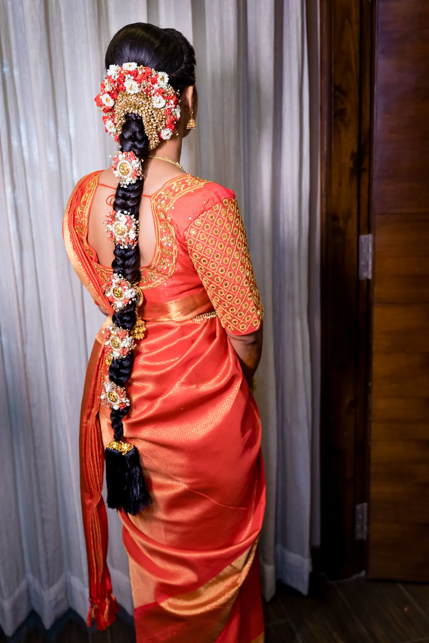 Medha seen from behind in an orange silk sari with a long braid of flowers