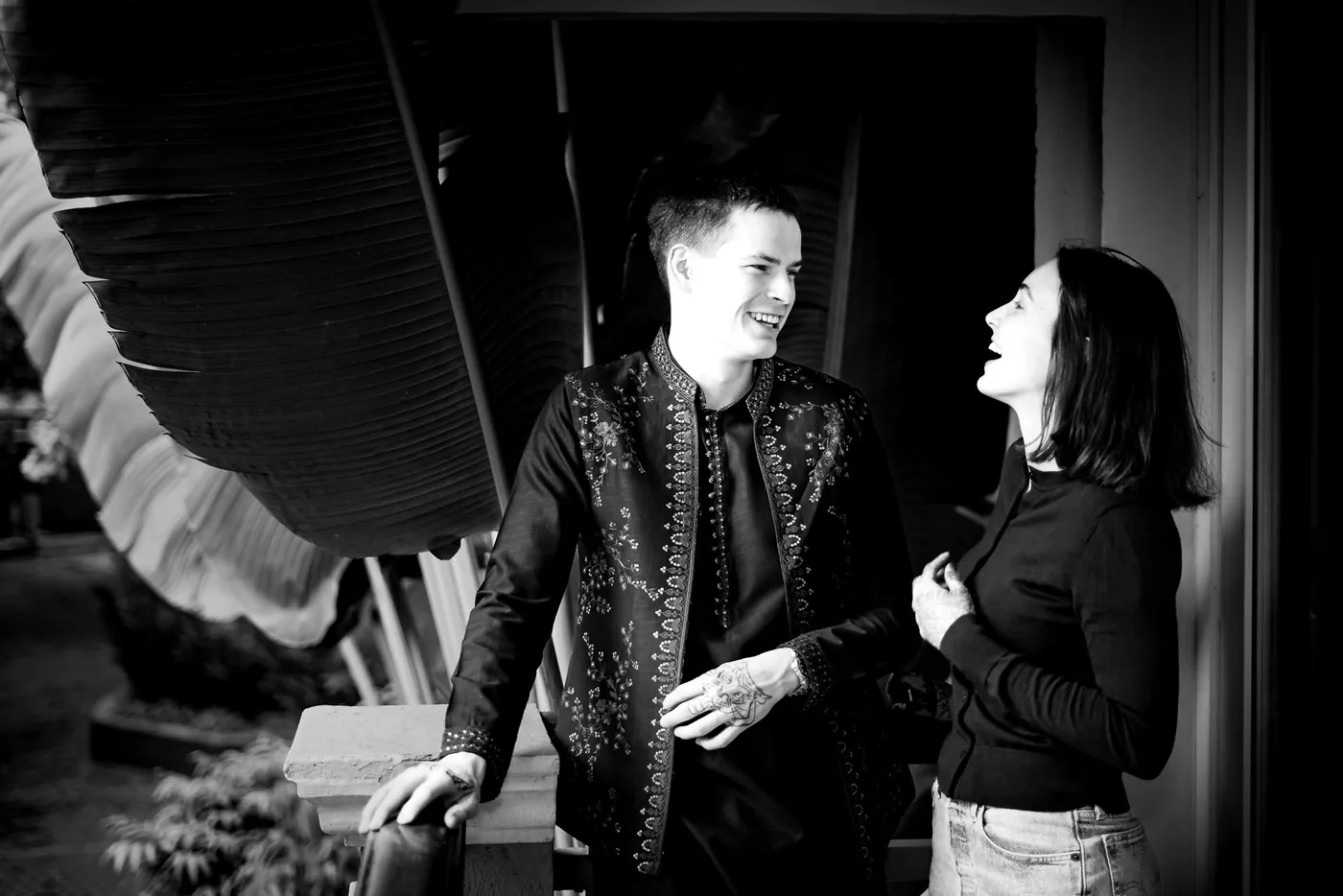 Black and white of Stefan laughing with a woman in a black top among large leaves