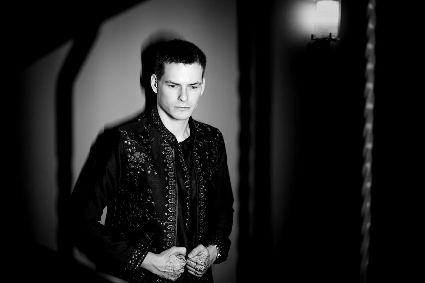 Black and white of Stefan under a harsh spotlight, adjusting the front of his embroidered jacket