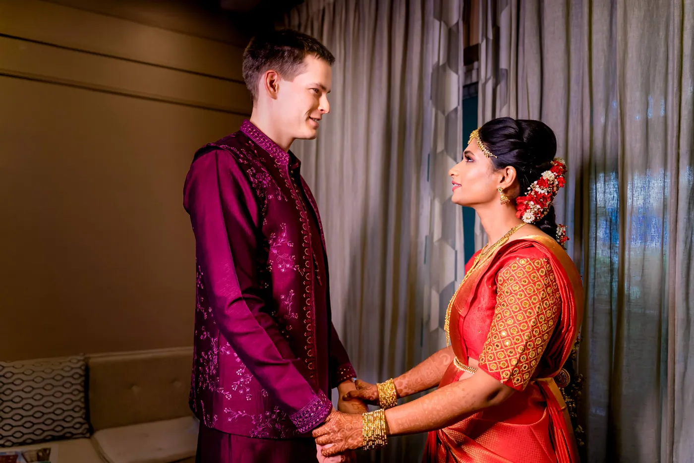 Medha and Stefan hold hands face to face by curtains, he in magenta and she in orange