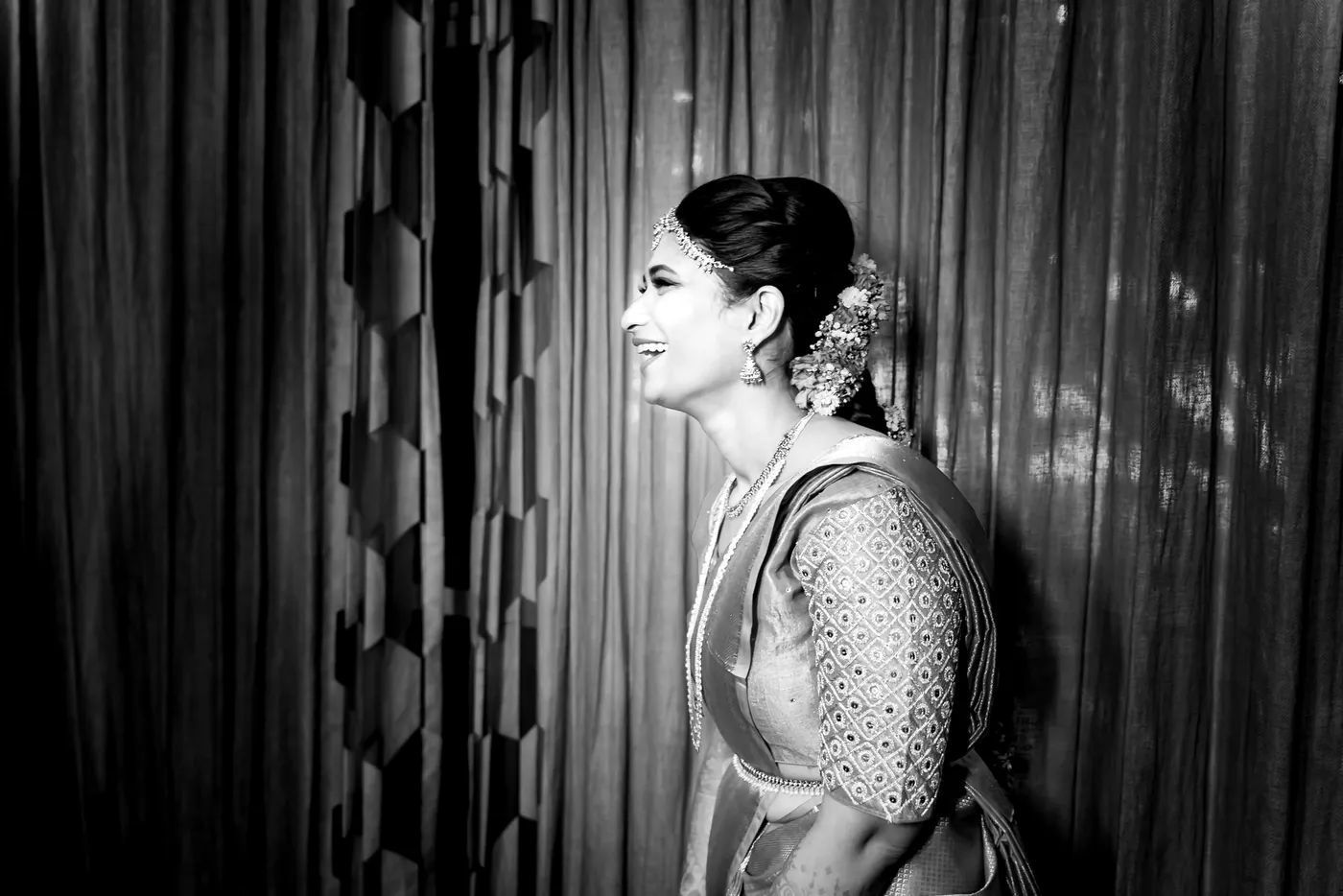 Black and white profile of Medha in a headpiece against a tall curtain