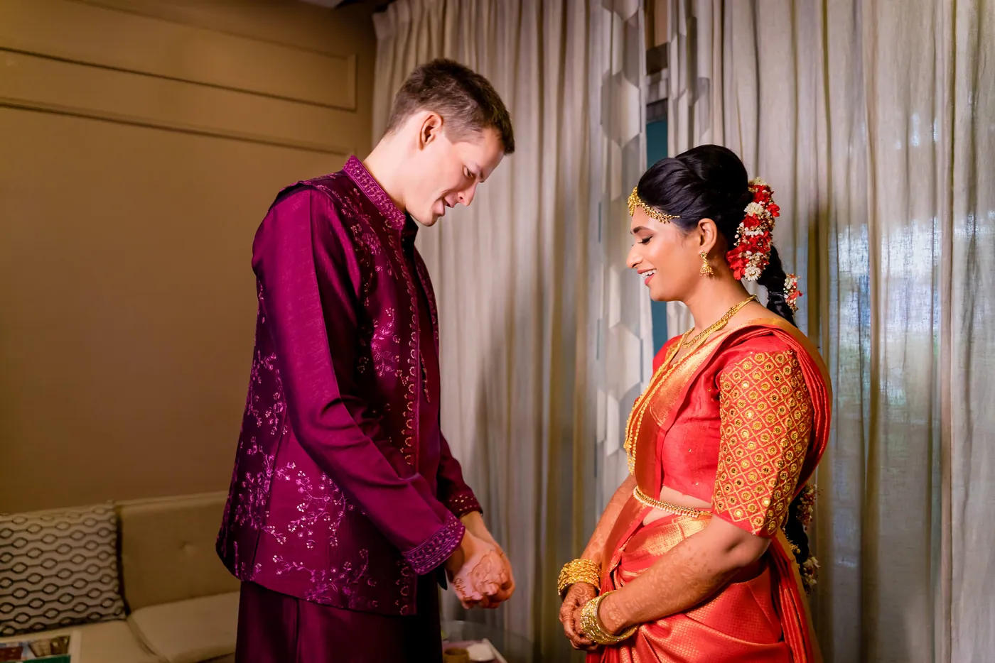 Stefan looks down toward Medha, who stands in an orange sari with flowers in her hair