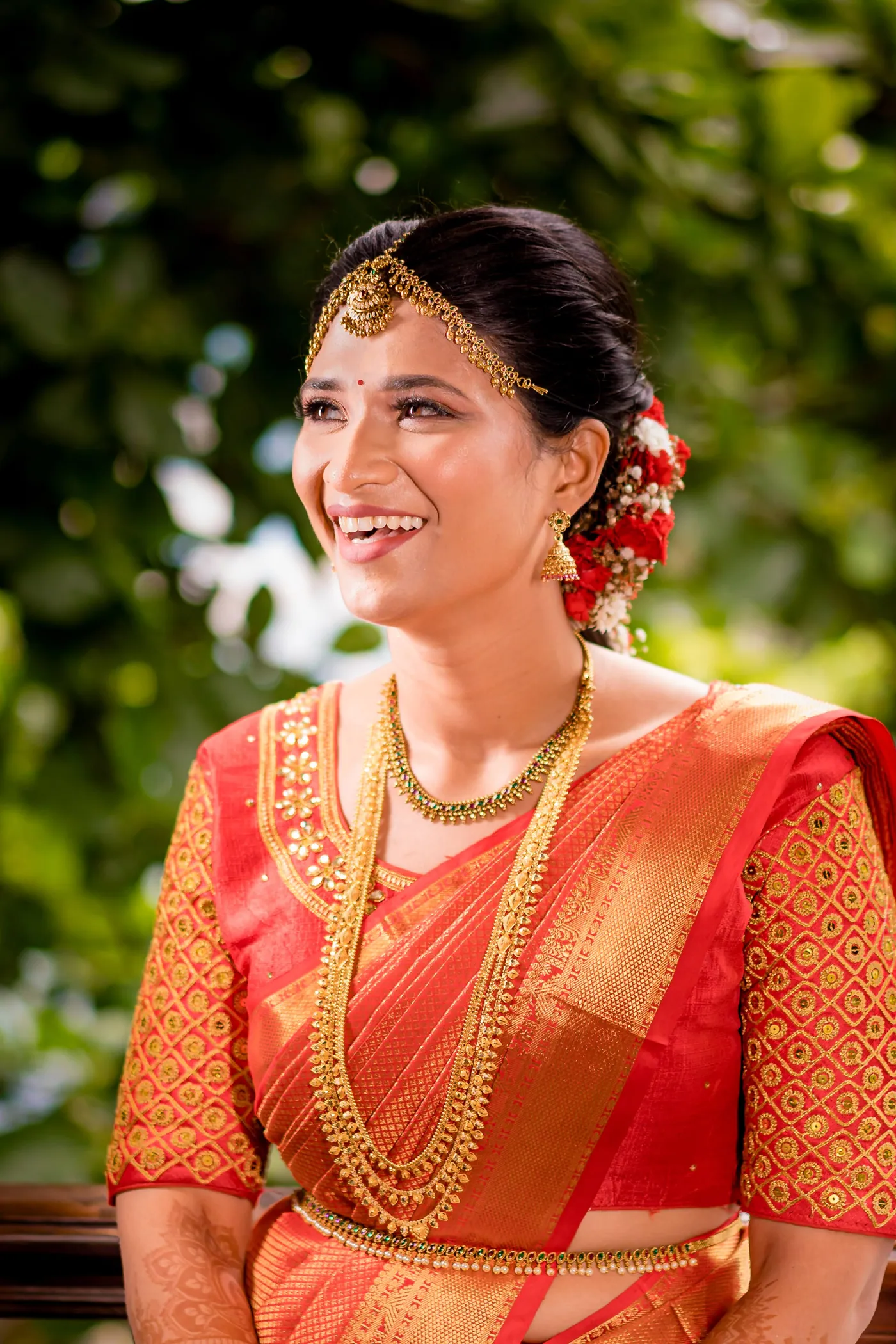 Medha laughs with her head tilted back in an orange sari with gold necklaces and flowers