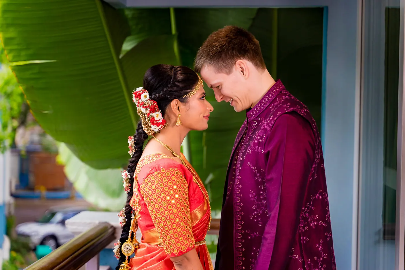 Medha and Stefan touch foreheads on a balcony, she in orange and he in magenta