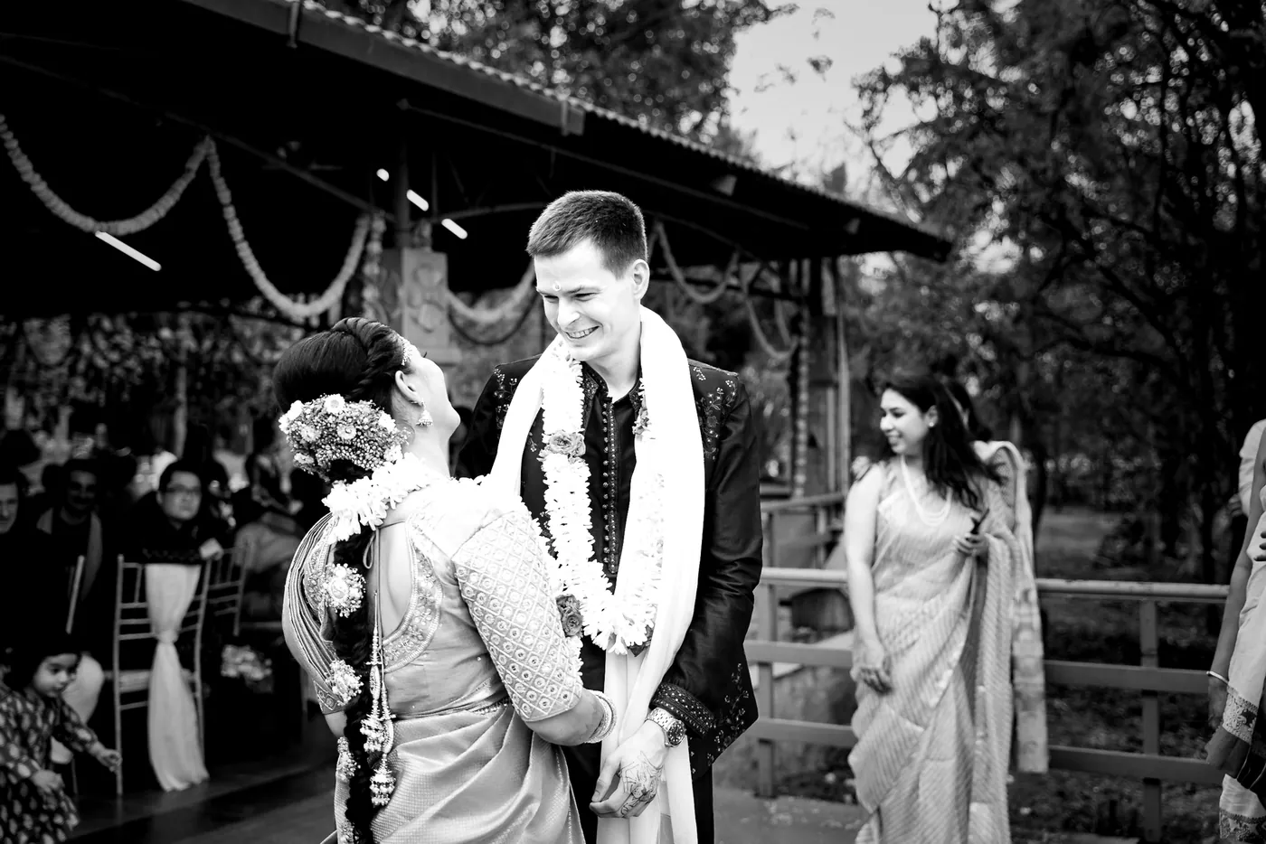 Black and white of Medha and Stefan laughing together in garlands on the deck