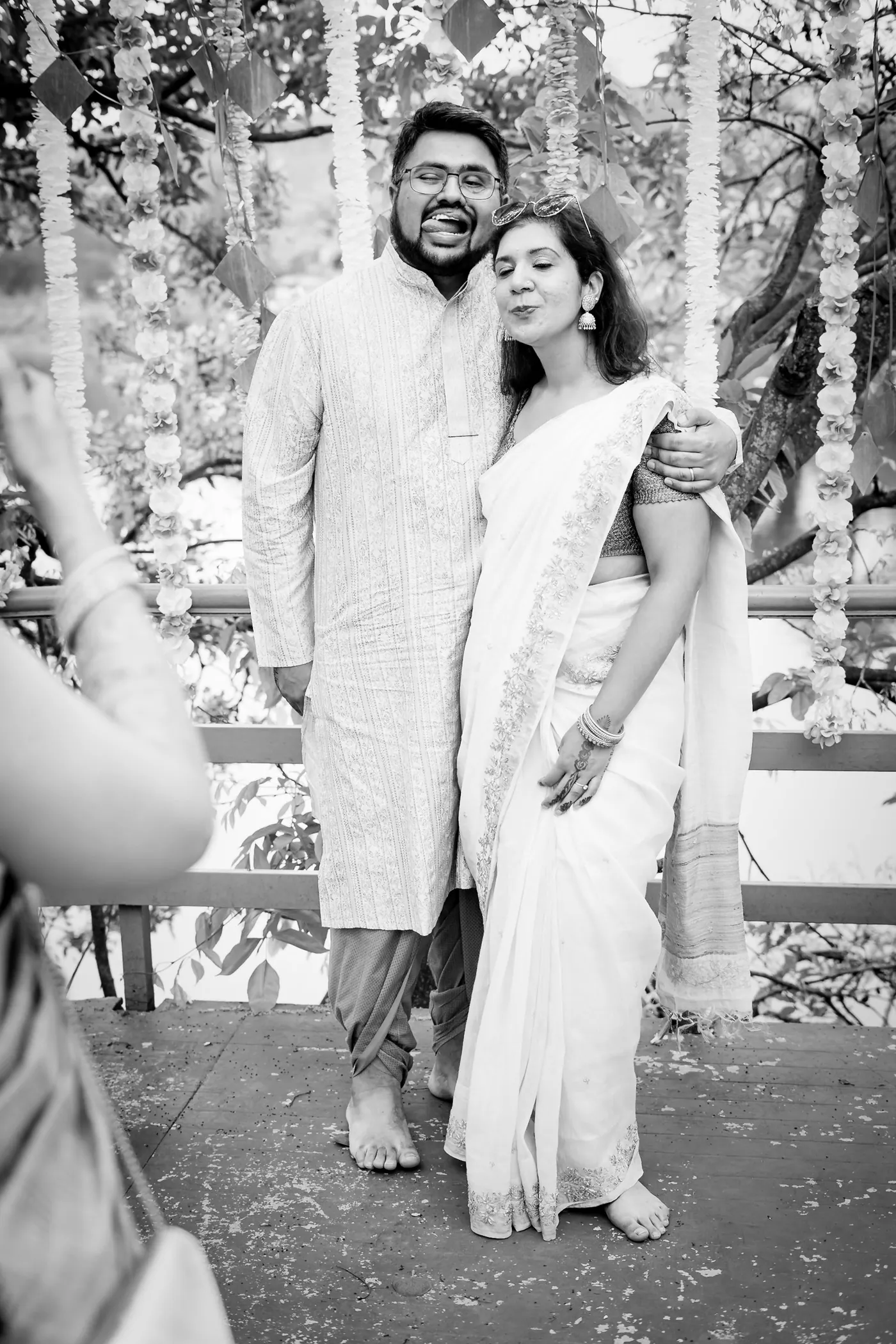 Black and white of a man and a woman hug on a deck in front of hanging flowers