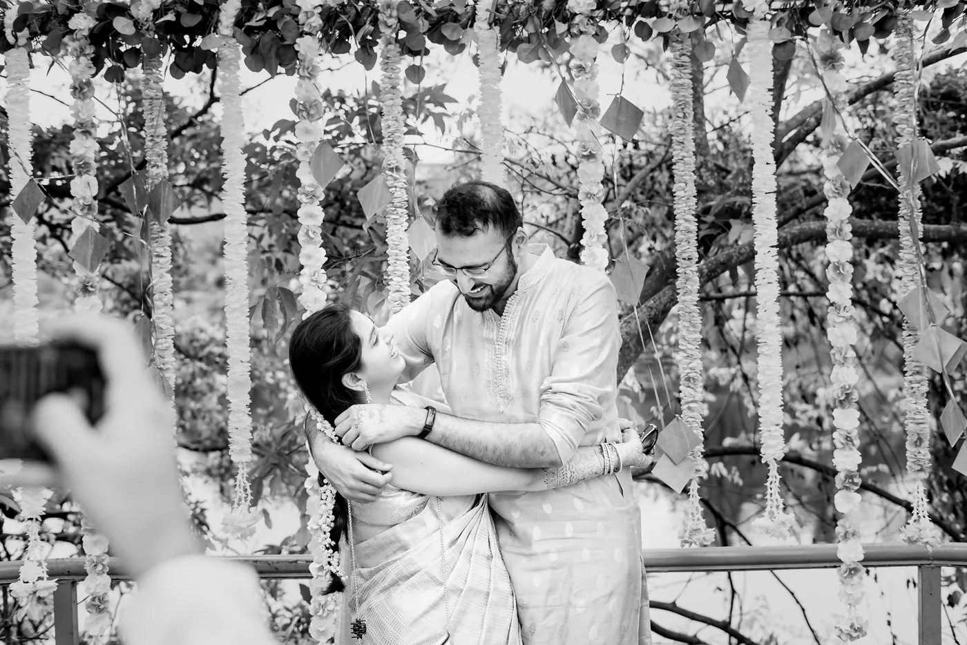 Black and white of friends embracing and playfully hugging among hanging flowers