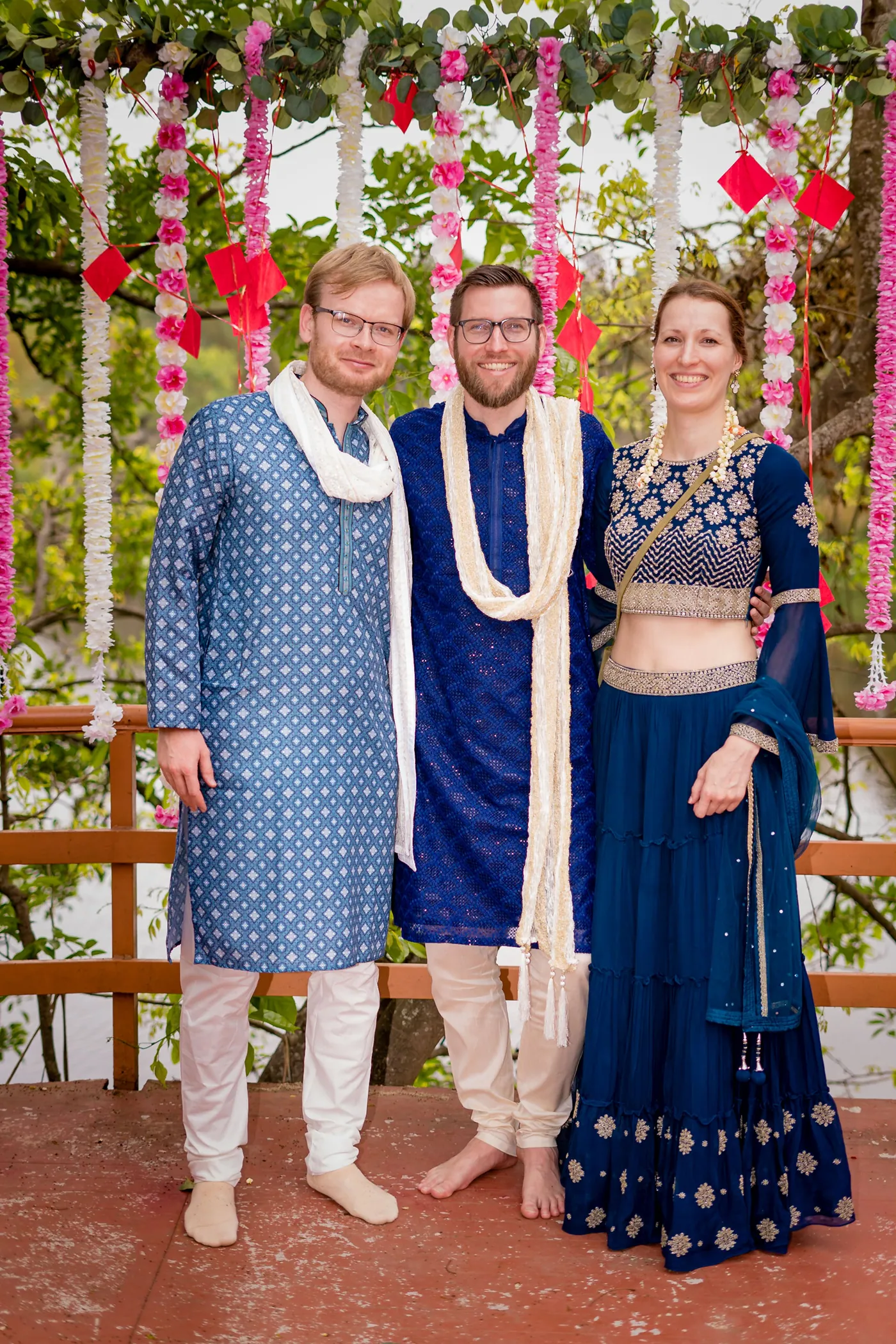 A man in blue and two friends in blue and navy pose in front of hanging flowers