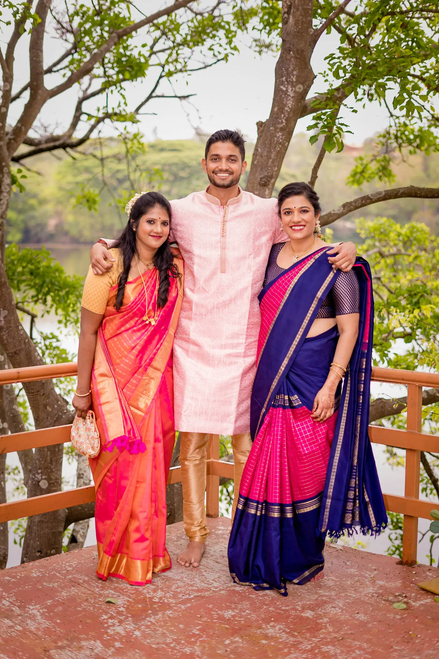 Three friends in pink and blue saris and cream pose with arms around each other