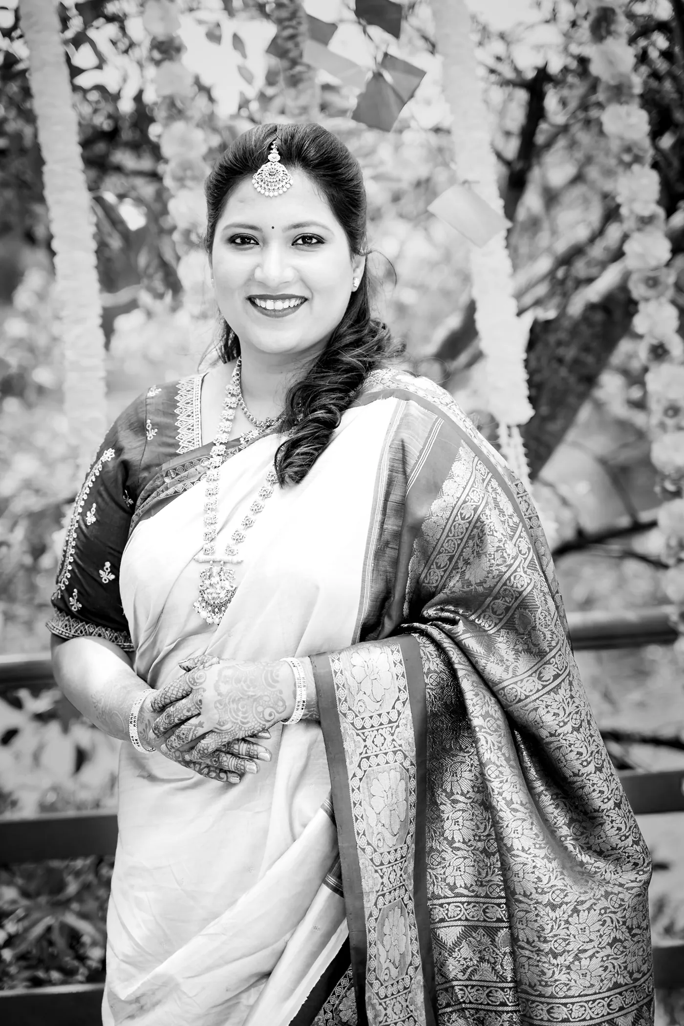Black and white of a woman in a headpiece and dark sari smiling warmly