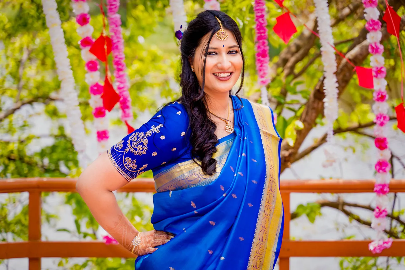A woman in a blue sari stands with a hand on her hip on a wooden deck