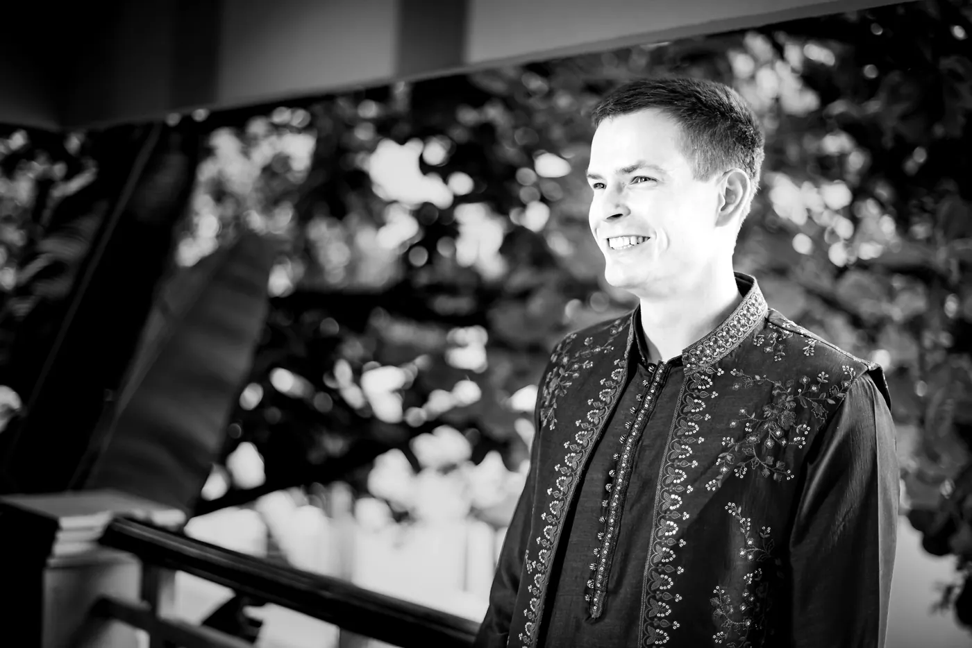 Black and white of Stefan smiling off to one side on a wooden balcony in his embroidered jacket