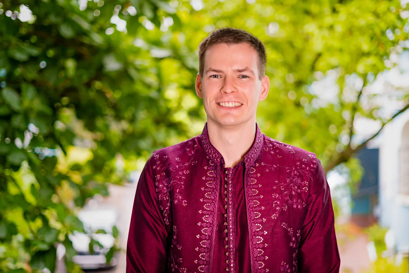 Close portrait of Stefan grinning in a magenta kurta against bright green leaves