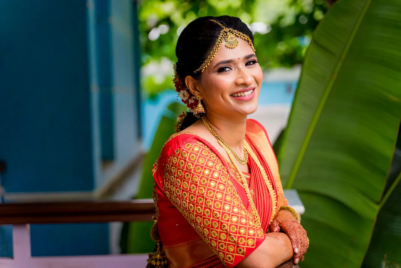 Medha laughs with her arms folded on a rail in front of banana leaves