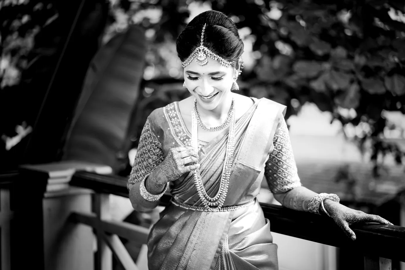 Black and white of Medha in a pale sari with layered necklaces laughing as she looks down at her hands
